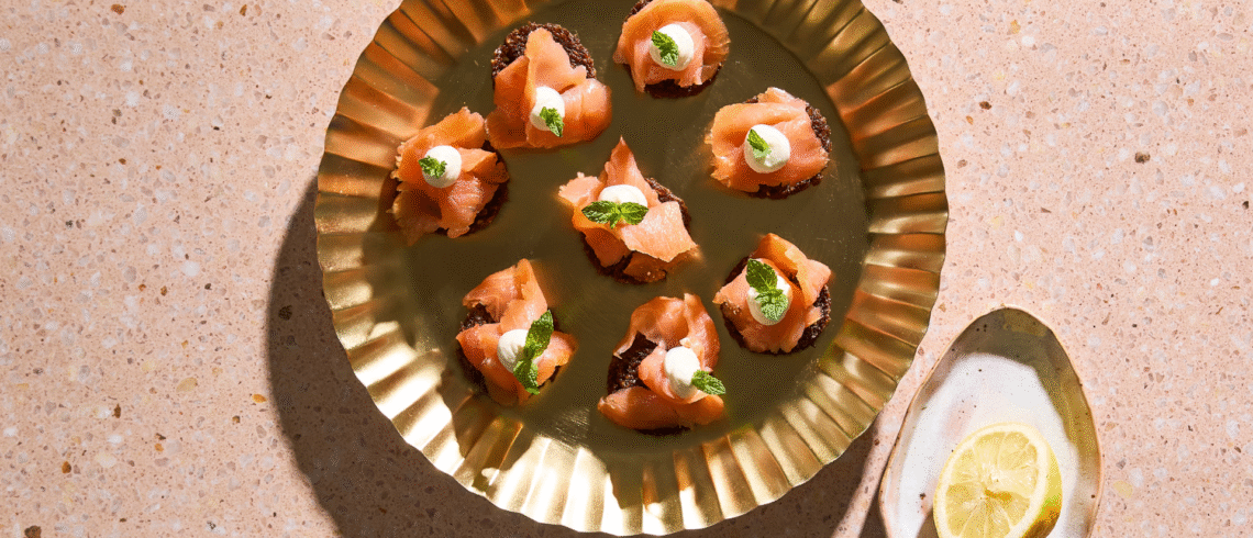 Små rugbrødsblinis med koldrøget laks, citroncreme og frisk dild.