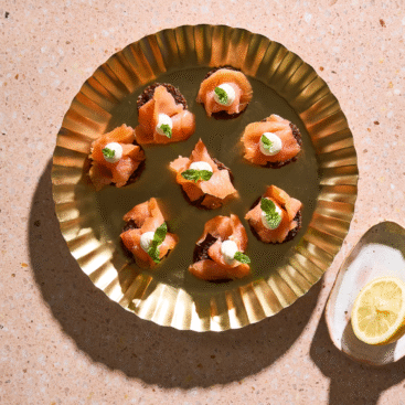 Små rugbrødsblinis med koldrøget laks, citroncreme og frisk dild.