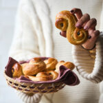 En person holder en kurv med luciabrød og løfter et enkelt brød op med den anden hånd.