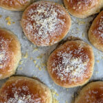 Nybagte juleboller med gylden overflade, penslet med appelsinsirup og drysset med appelsinskal og flormelis.