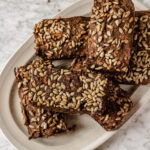 Skiver af skolerugbrød med gulerødder og solsikkekerner lagt på hvid tallerken set oppefra.